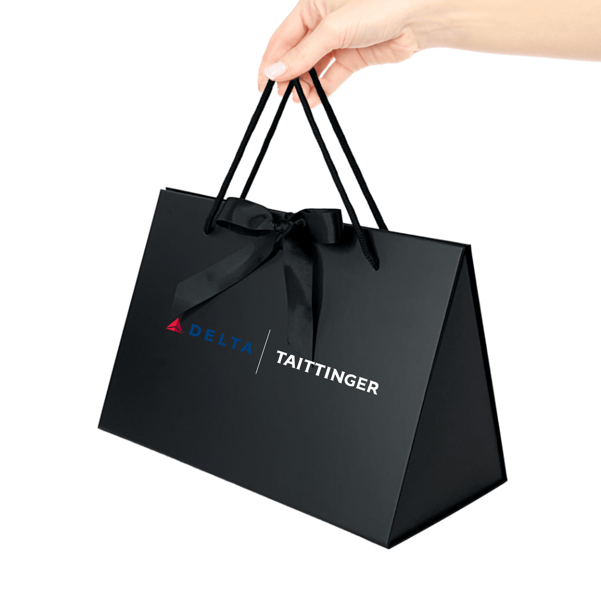 Black gift bag with Delta and Taittinger logos held by a hand on a white background